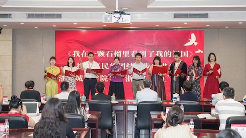 这张照片是阿曼参加浙里石榴红校园驿站揭牌仪式时和来自政府、高校、企业、退役军人的各民族师生一起朗读《我在一颗石榴里看到我的祖国》，这首诗歌表达出各民族像石榴籽一样紧紧抱在一起的中国力量。